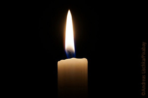 Eine brennende Kerze vor dunklem Hintergrund.