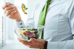 Man in blue shirt and green tie eats salad from a glass bowl