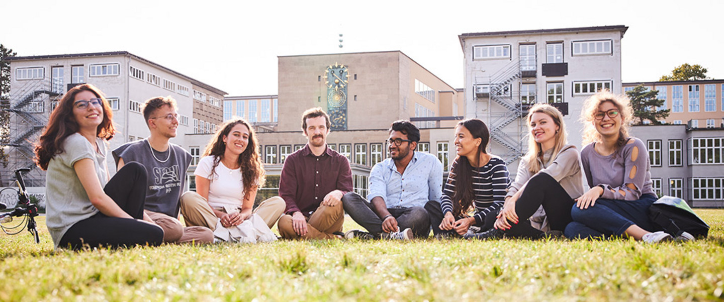 Studierende im Halbkreis sitzend auf der Uniwiese hinter dem Hauptgebäude der Universität zu Köln
