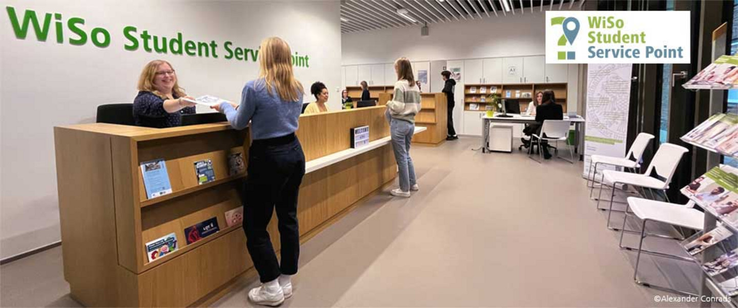 Young people stand and sit at four reception desks in the WiSo Student Service Point, receive information and documents in a relaxed exchange. Text (Logo): WiSo Student Service Point.