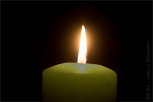 A candle flame shines into a dark background.