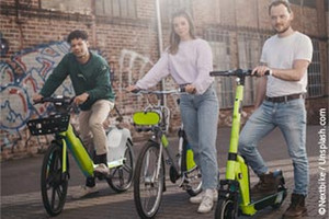 Three people pose with different rental bikes and a scooter