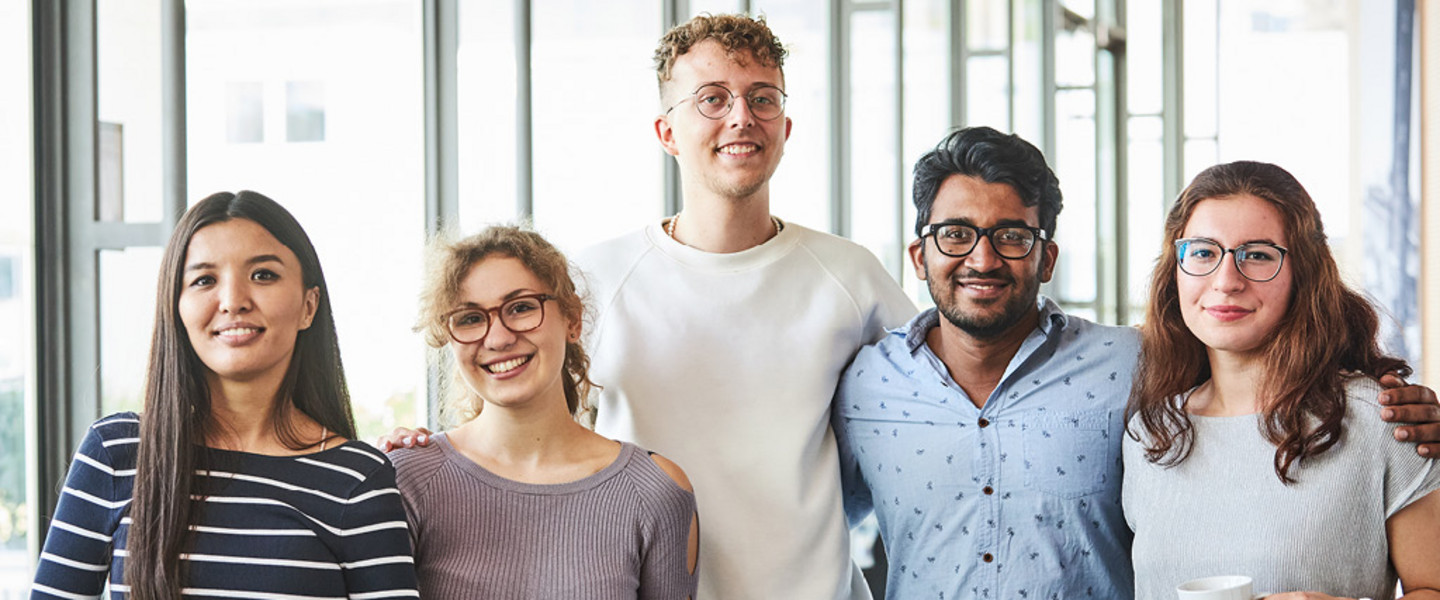 Bachelor of Business Administration of the University of Cologne - five smiling colleagues - young creatives - in front of a glass wall in the office.