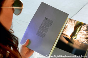 angeschnittene Frau mit Sonnenbrille schaut in eine Broschüre mit dem Foto eines funkensprühenden Bohrers.