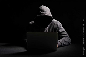 Jemand in einem Kapuzenpulli im Dunkeln hinter einem Laptop, das Gesicht unkenntlich.