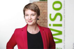 Prof. Dr. Naeve-Stoß in a red blazer, smiling. In front of a brick wall, with the WiSo logo in the background.