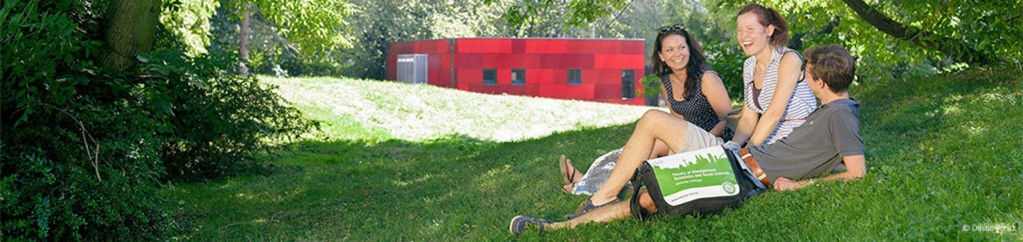Drei jungeMenschen entspannt in einem Park gruppiert, ein rotes Gebäude im Hintergrund