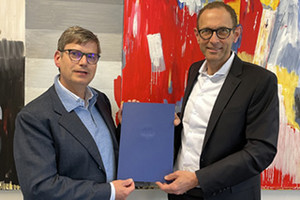 Christoph Wolff und Ulrich Thonemann präsentieren gemeinsam Wolffs Ernennungsurkunde zum Honorarprofessor vor einem abstrakten Gemälde.