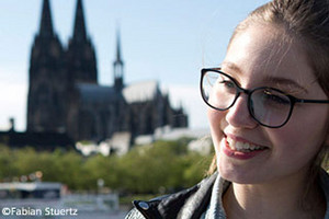 A smiling young woman in front of the Rhine with a view on cologne cathedral