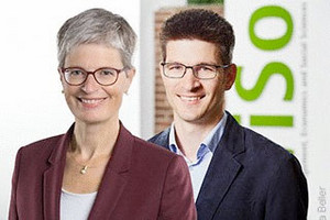 Prof. Dr. Marita Jacob und Prof. Dr. Clemens Kroneberg, im Hintergrund der WiSo Schriftzug und eine Backsteinmauer. Beide lächeln. 