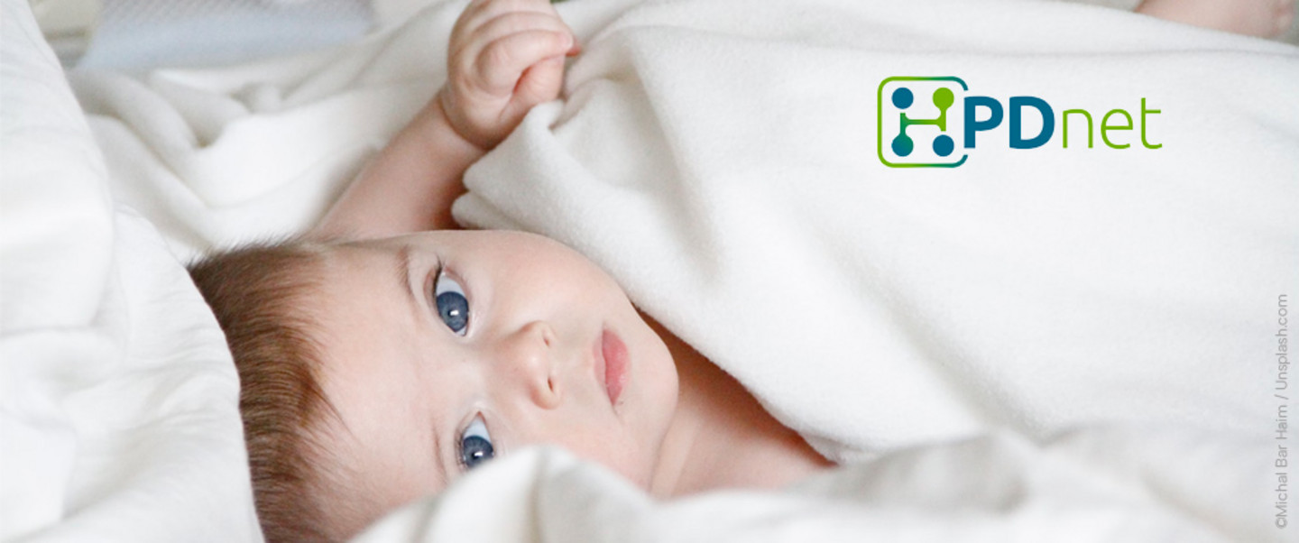 A blue-eyed toddler lies in white bedding and looks diagonally upwards out of the picture towards the viewer. Top right HPDnet logo (green-blue lettering with an inital "H" encompassing network nodes).