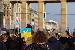 Eine Frau mit einem Poster der ukrainischen Flagge und andere Menschen auf der Straße