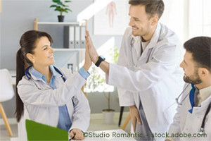 A team of three doctors sitting at a table celebrating a joint success, a female doctor and a male doctor high-five each other - study by the University of Cologne examines motivation through internal rankings