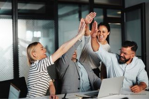 Vier Personen, sitzen zusammen in einem Büro an einem Tisch schauen sich lächeln an und schlagen ein.