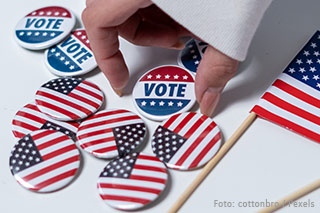 weibliche Hand hebt einen Wahlbutton zur Wahl in den USA aus einem Haufen heraus