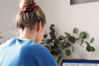 Eine junge Frau in einem blauen Pullover schaut auf einen Laptop