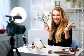 long-haired blonde beauty influencer sits at a make-up table in front of the camera, presenting lipsticks.