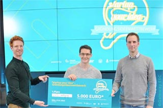 Moderator Andreas Klein, company founder Bernhard Röck and Professor Dr Christian Schwens jointly hold the winner's cheque in front of a projection screen with the logo of the "startup your idea" competition of the Gateway ESC and the WiSo Faculty