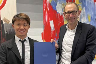 Professores Ziyue Li and Ulrich Thonemann togehter holding an appointment dokument in front of an abstract painting
