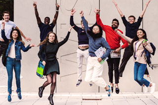 A group of nine students jump up in front of the entrance of the WiSo building