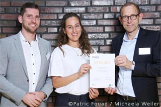 The Dean of the WiSo Faculty Prof. Ulrich Thonemann wih scholarship holder Sarah Gadhoum and sponsor Christian Maurer (MLP) in front of a brick-wall
