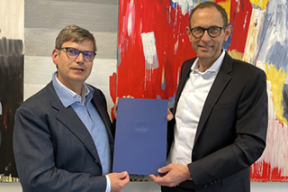 Christoph Wolff and Ulrich Thonemann jointly present Wolff's certificate of appointment as honorary professor in front of an abstract painting.
