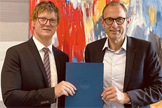 Professor Dr. Thomas Wagner and Wiso Dean Ulrich Thoneman in front of an abstract painting, holding Professor Wagner's certificate of appointment as honorary professor.