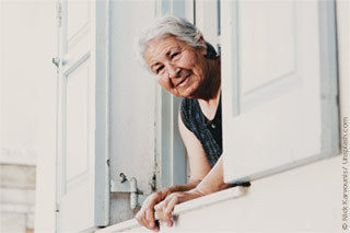 Ältere Dame schaut lächeln aus dem Fenster.