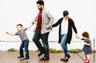A family of four people. Walking on a sidewalk holding hands.