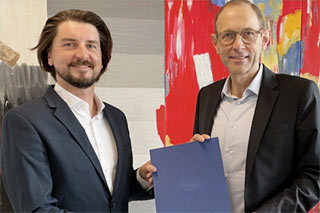 Auf dem Bild sieht man Prof. Thonemann und Dr. Thomas Scholdra, die gemeinsam ein Papier halten und in die Kamera schauen.