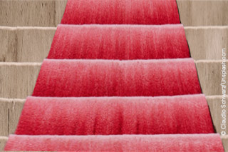 EIn roter Teppich auf vir aufwärts führenden Stufen.