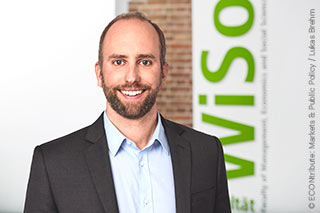 Prof. Dr. Sebastian Siegloch in front of a half-white, half-brick wall with a WiSo lettering