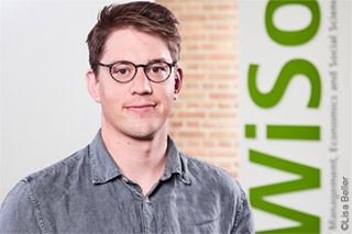 Prof. Dr Christopher Roth in a blue-grey shirt in front of a brick wall with WiSo lettering