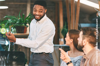 A confident entrepreneur gives a presentation to his co-founders in a start-up environment surrounded by plants and modern office furnishings.