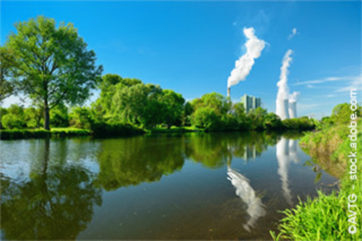 Kraftwerk mit Kühltürmen, die Dampf ausstoßen, hinter einer grünen Flusslandschaft unter klarem, blauem Himmel.