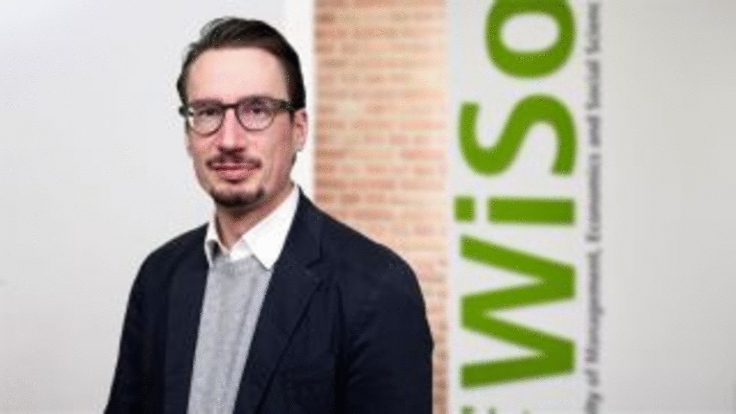 Prof. Dr. Markus Weinmann, professor of Business Analytics at the Faculty of Management, Economics and Social Sciences. He is wearing glasses, mildly smiling towards the camera. A red brick wall in the background and the logo of the WiSo Faculty.